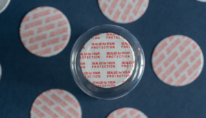 Vista cercana de un sello sensitivo tipo pressure sensitive con impresión “Sealed for your protection” en inglés, adherido a la boca de un frasco. Producto de seguridad desarrollado por Sellaempaq para proteger medicamentos, suplementos y productos cosméticos contra manipulaciones.